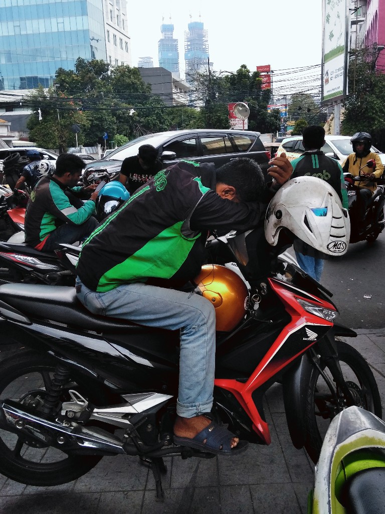 Tukang ojek Gojek duduk tertidur di atas motor di depan Stasiun Gondangdia Jakarta 